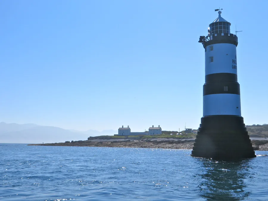 The black-and-white Trwyn Du Lighthouse standing on its rock off Penmon Point, the low headland and its white pilot houses behind, at the eastern tip of Anglesey.