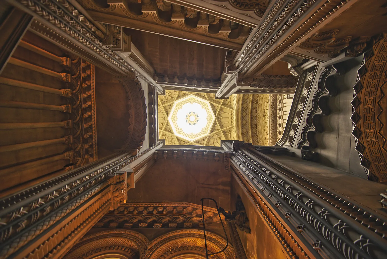 Looking up through the ornate carved stonework of Penrhyn Castle's Grand Staircase to a decorated lantern ceiling.