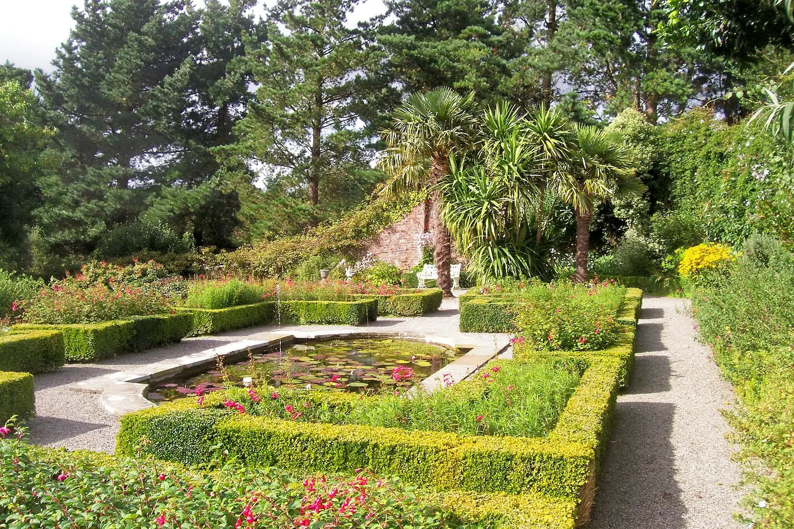 The Terraced Garden at Penrhyn Castle, with box hedging, a lily pond and palm trees against the old brick garden wall.