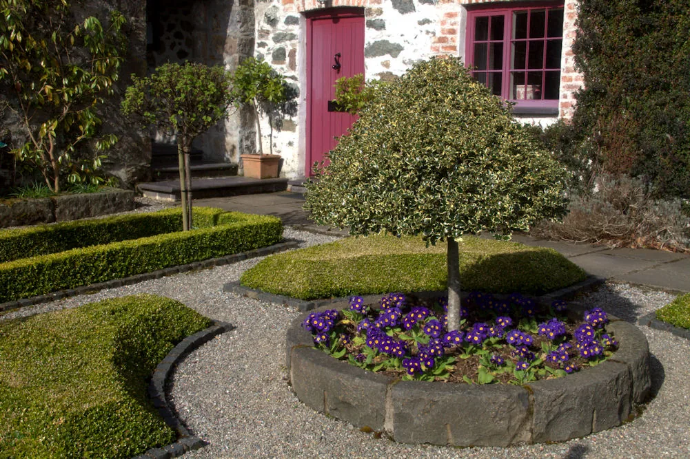 A wide view across the planted gardens at Plas Cadnant, lawns and borders running down toward the wooded valley.