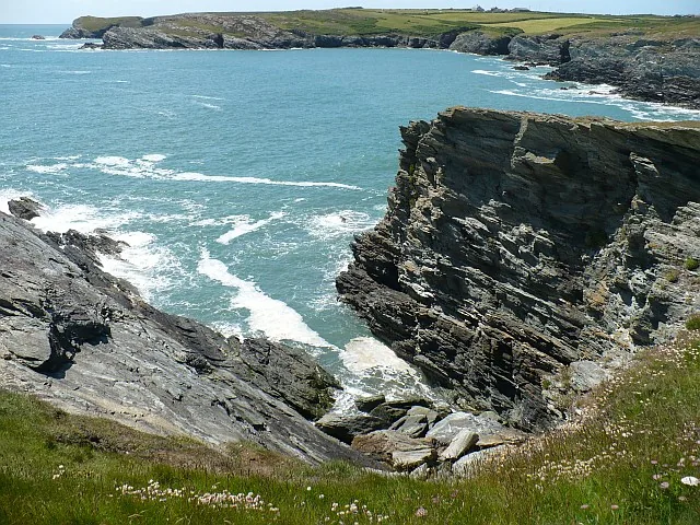 Rocky cliffs and clear turquoise water near Porth Dafarch, waves breaking against dark rock.