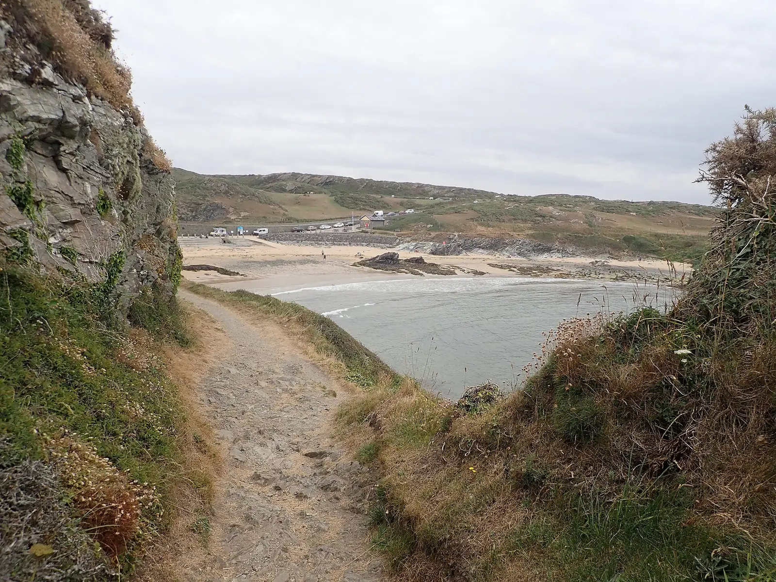 The coast path descending toward Porth Dafarch beach, cliffs on one side and the bay opening ahead.