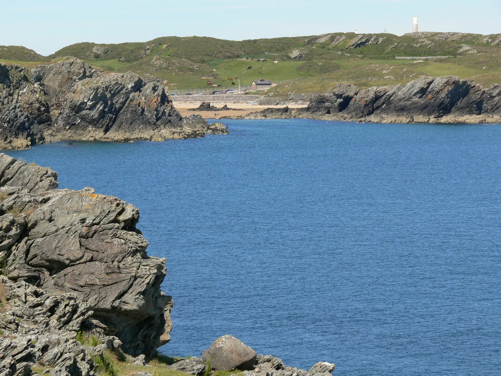 Porth Dafarch seen from the cliffs at Graig Lwyd to the south-east, deep blue water below a low rocky headland.