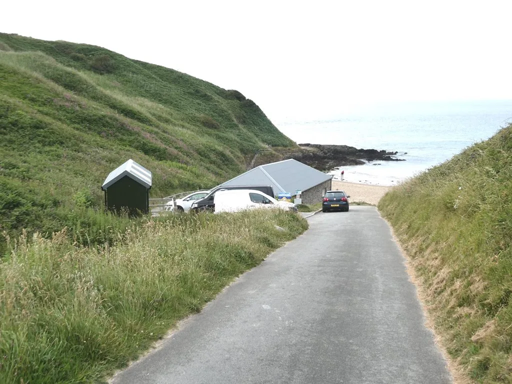 The steep access lane down to Porth Oer, with the car park building and the beach visible ahead.