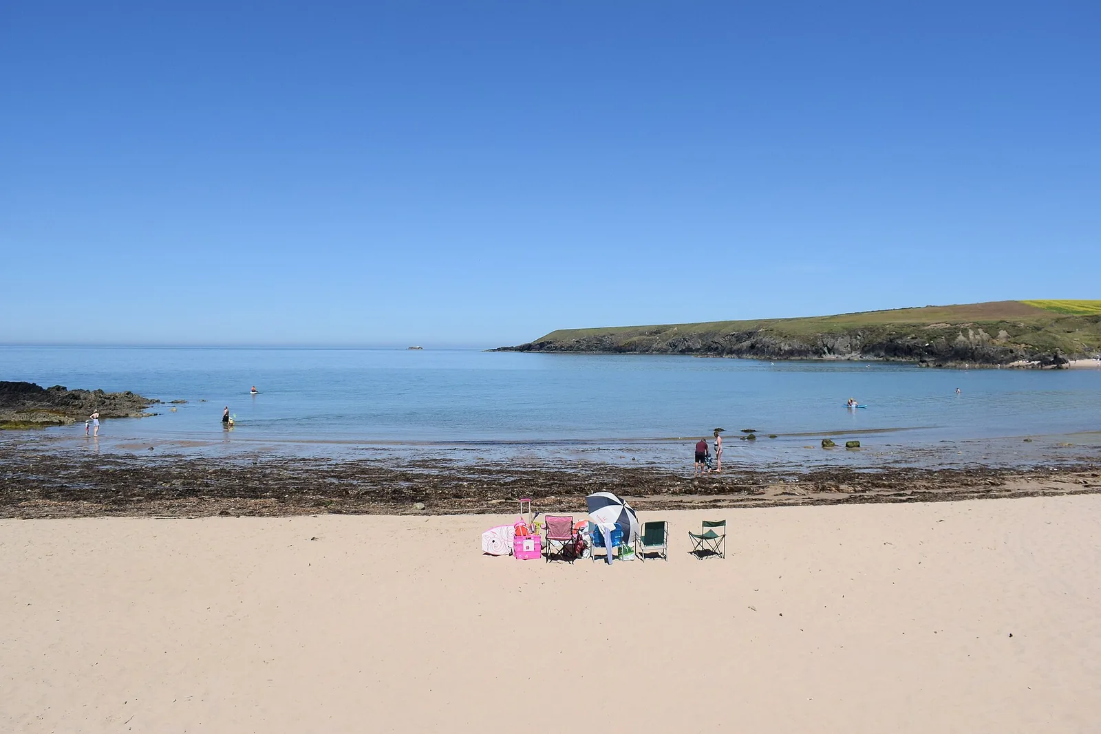 Porth Oer beach at low tide, seen from the sand, with a headland closing the cove on the far side.