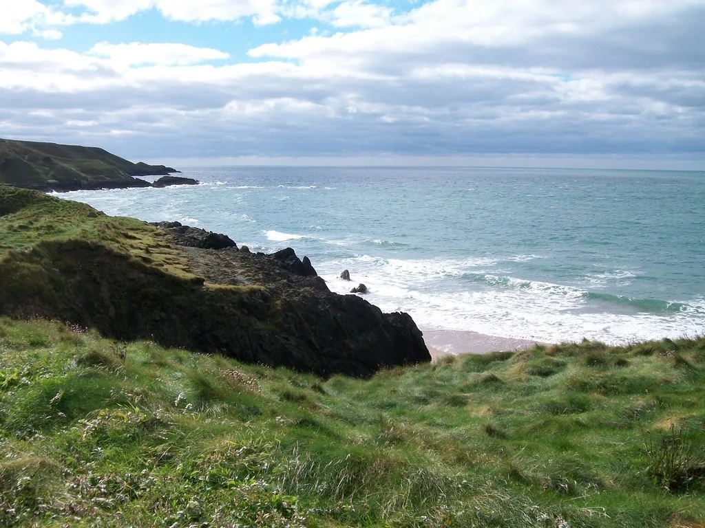 Dark rocky cliffs at Porth Oer with waves breaking against the shore.