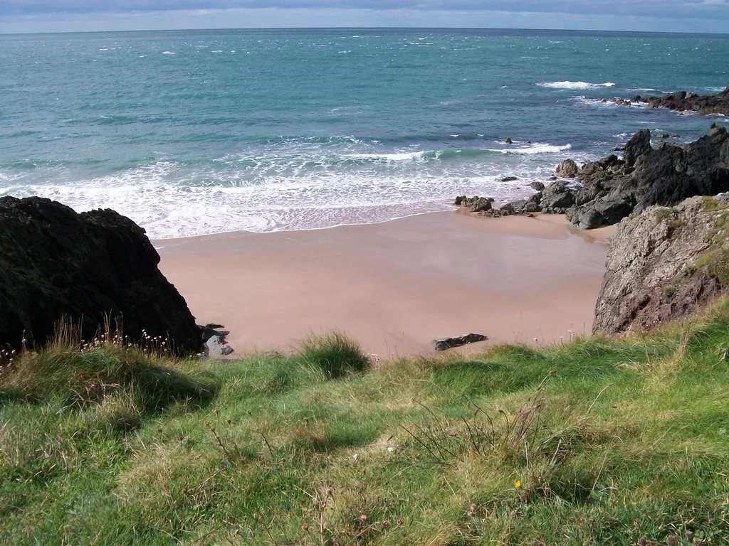 A sandy stretch of Porth Oer's beach with rocks at the water's edge.