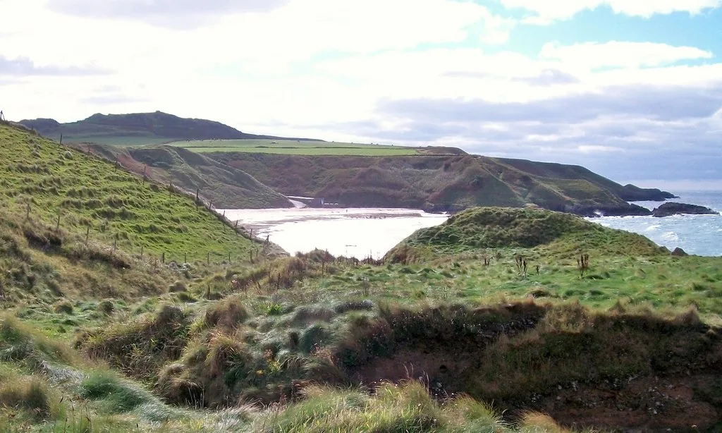A wide, curving stretch of the beach at Porth Oer, cliffs and farmland rising behind.