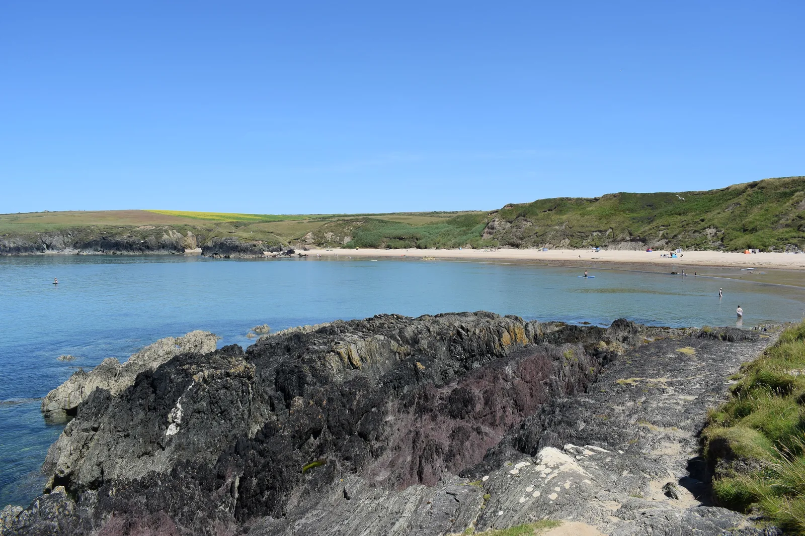 Dark coastal rocks in the foreground with the whole curve of Porth Oer's cove beyond.