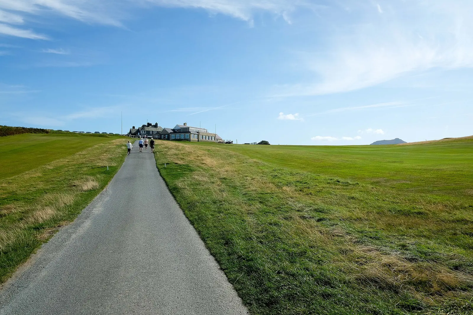 Walkers on the paved coast path crossing Nefyn & District Golf Club, the clubhouse ahead.
