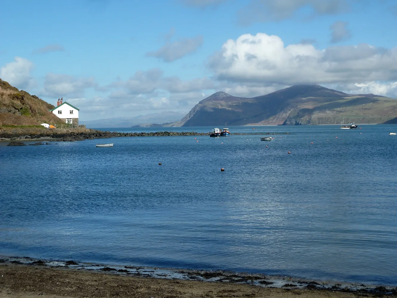 Porth Dinllaen bay at low tide, a white cottage on the rocks and Yr Eifl hills beyond.