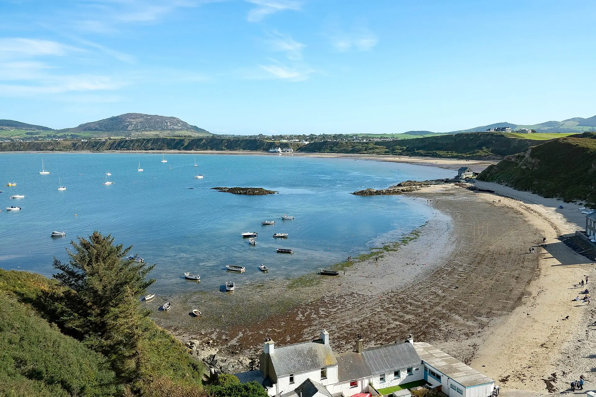 The curved beach and whitewashed cottages of Porthdinllaen on the Llŷn Peninsula, the fishing headland reaching into a calm bay.