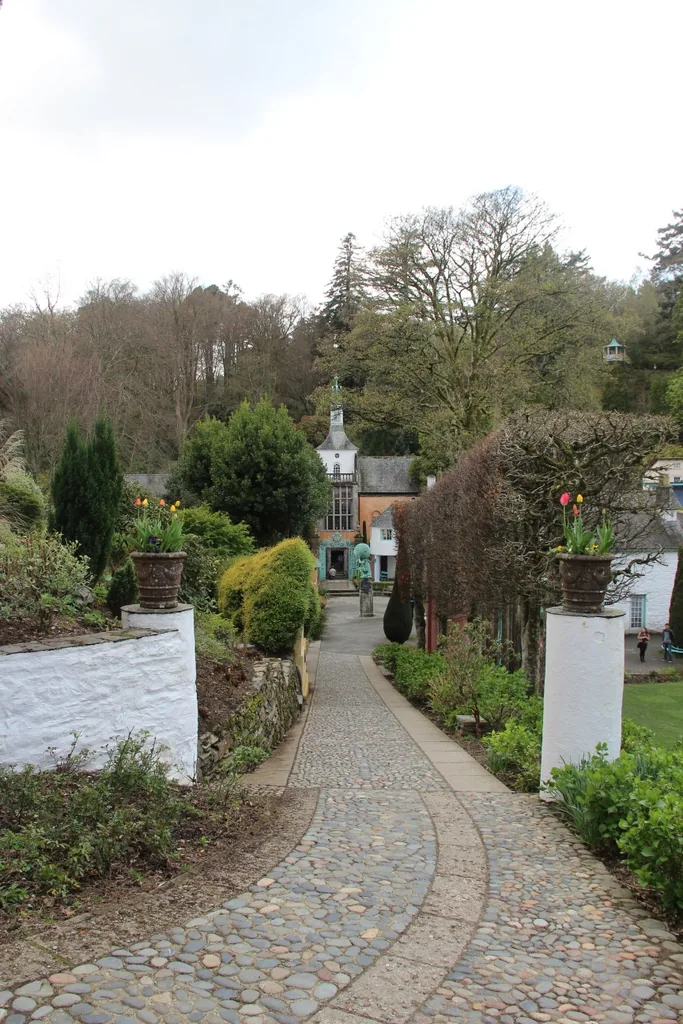A cobbled garden path lined by white walls and flower urns, leading towards a village building at Portmeirion.