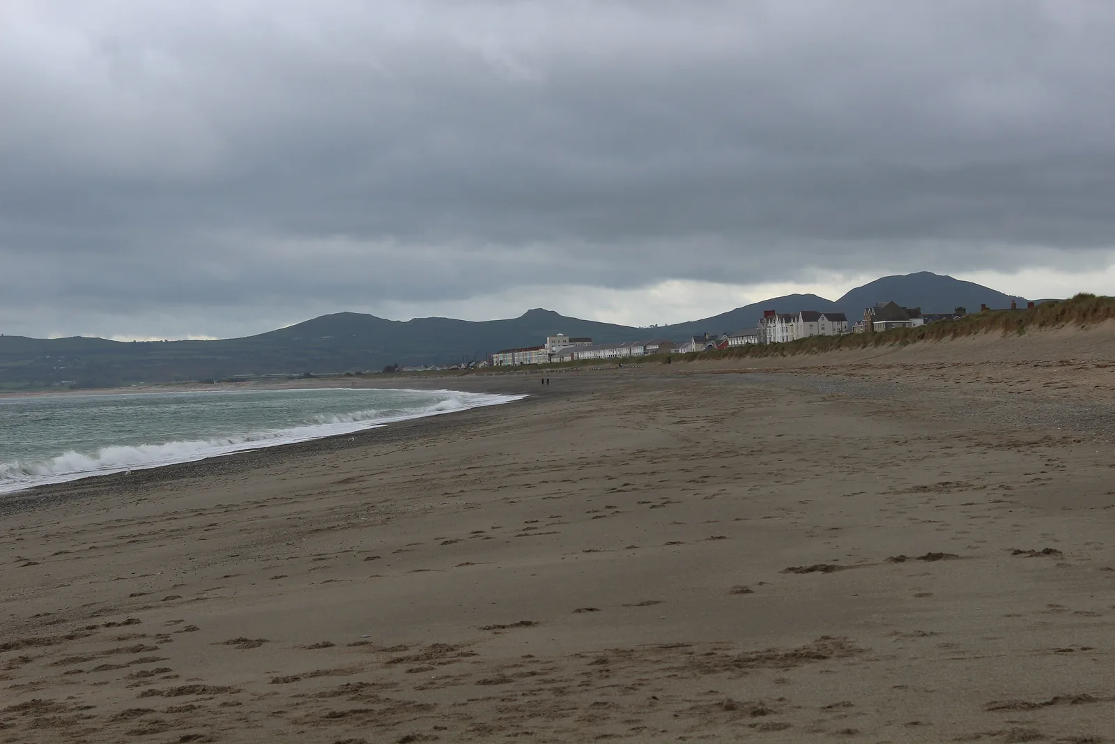 South Beach at Pwllheli, wet sand curving away to the West End terraces with the hills of the Llŷn behind