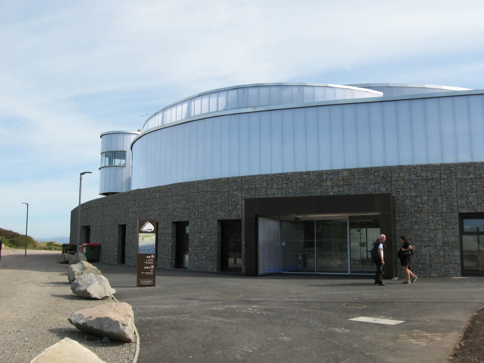 The curved translucent drum of Plas Heli above its stone-gabion base, with the entrance doors at ground level