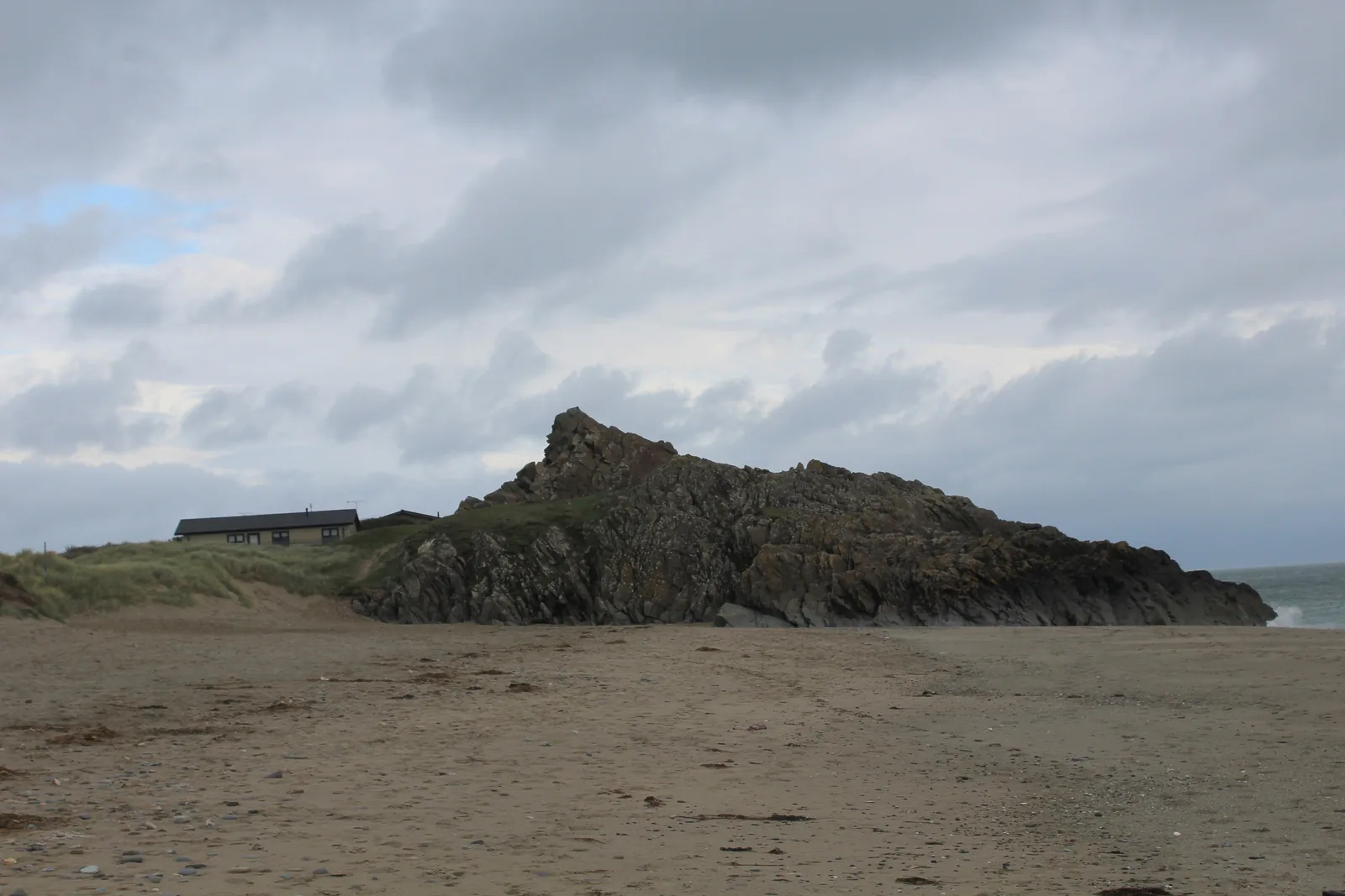 Carreg yr Imbill rising from the sand at the harbour mouth, its quarried faces dark under a heavy sky