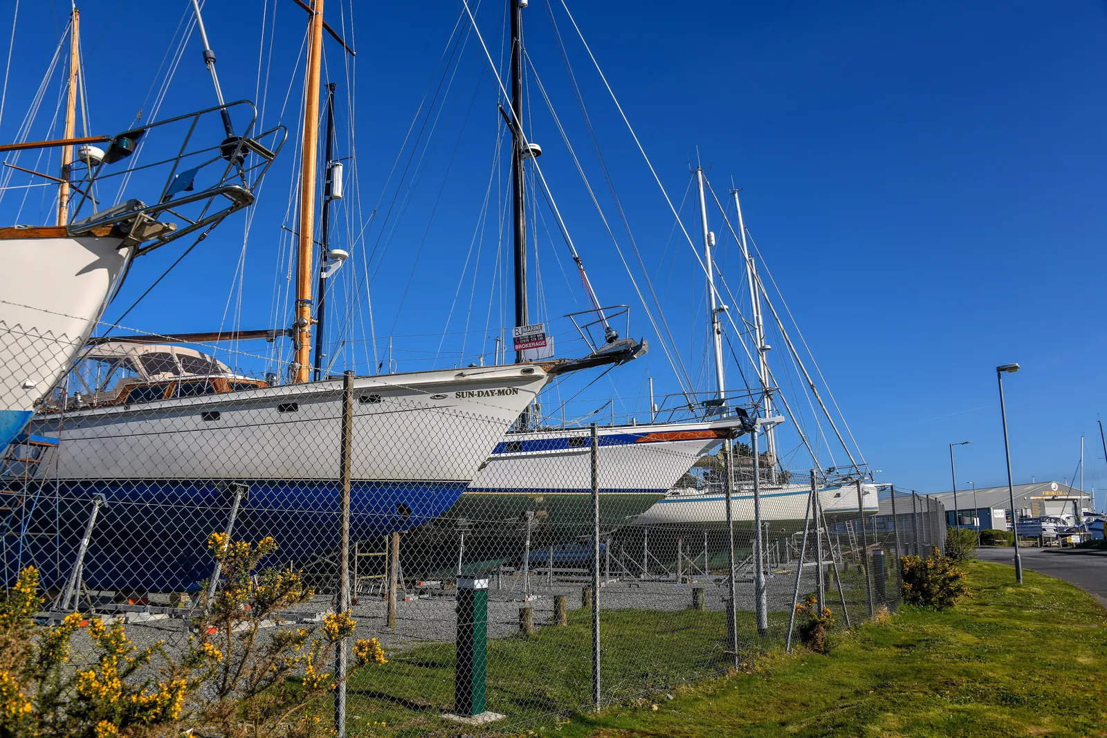 Yachts standing ashore on cradles inside a fenced boatyard at Pwllheli under a clear blue sky