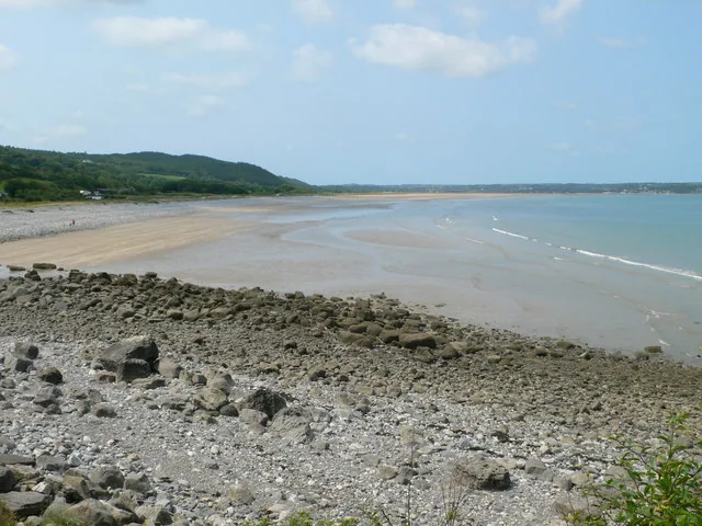 A rocky foreshore giving way to wide sand and sea at Red Wharf Bay, Anglesey, with a headland in the distance.