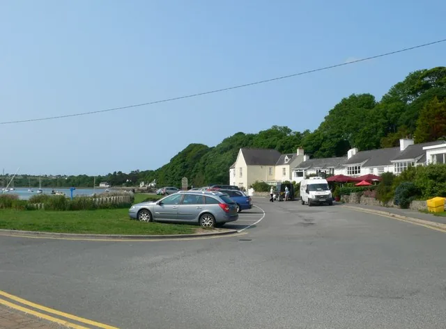 The small parking and village area near the Boathouse at Red Wharf Bay, with the tidal water and a wooded headland behind.