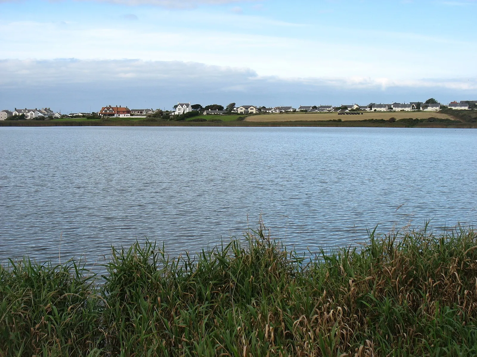 Llyn Maelog, the lake behind Rhosneigr's dunes, with village houses visible on the far shore