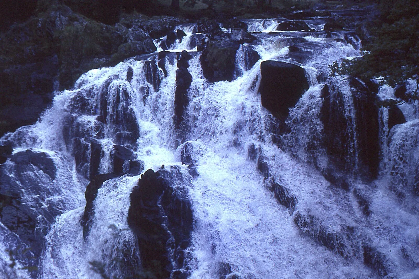 A 1964 photograph of Swallow Falls, the water dropping over the same dark rock in cooler tones.