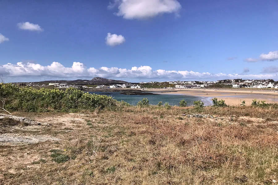 Trearddur Bay's sandy main beach on Holy Island, with the village and hills visible across the water.