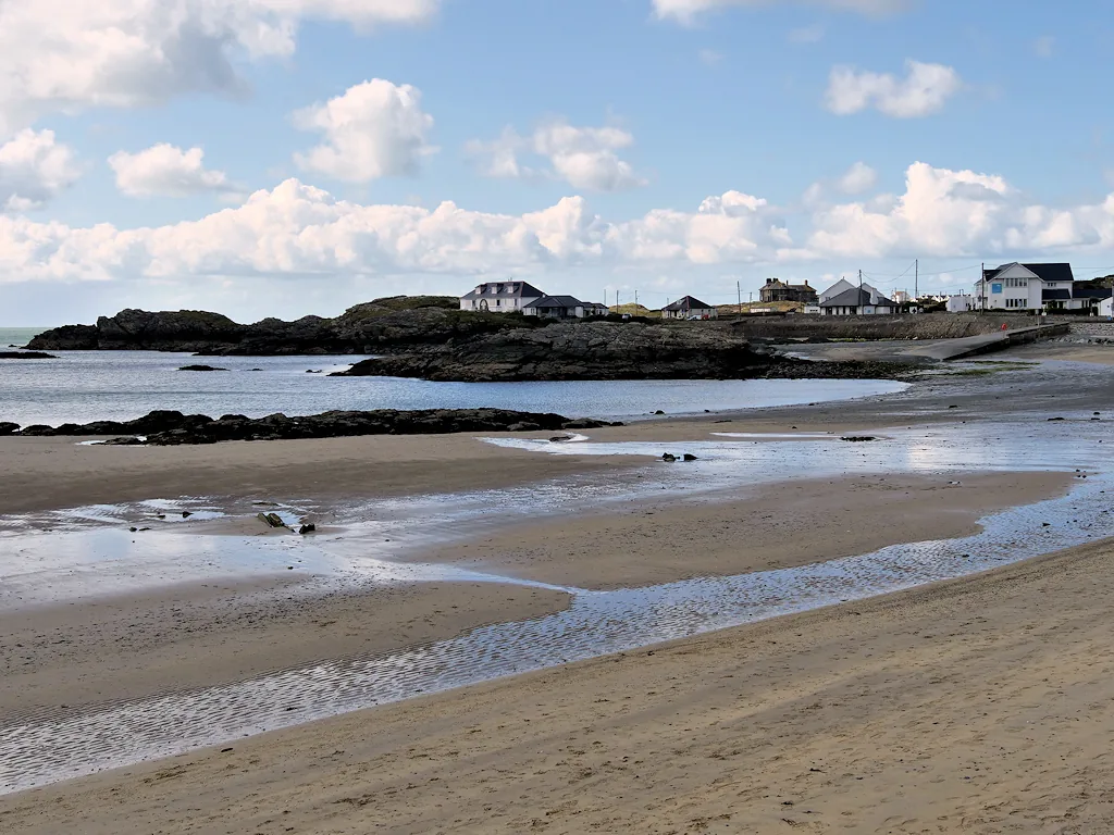 Towyn y Capel beach at low tide, with the village and hills visible across the water.
