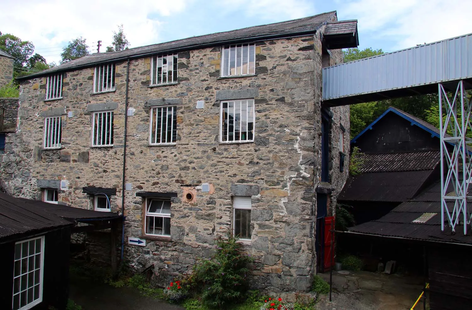 The stone mill buildings at Trefriw Woollen Mills seen from the yard, with the covered walkway crossing above