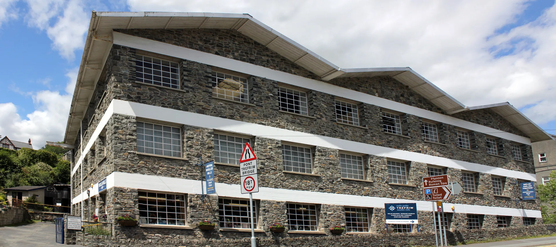 Trefriw Woollen Mills, a long three-storey stone building with white-banded floors, standing directly on the main road through the village