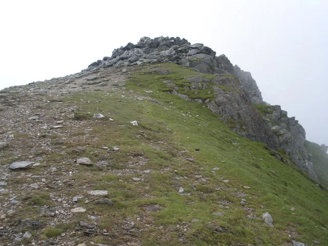 The cairn-topped summit crest of Y Garn in cloud, with a stony ridge rising to the cairn and the ground beyond lost in mist