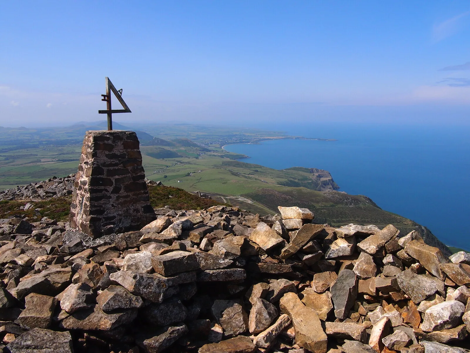 The trig pillar and block cairn on the summit of Garn Ganol, with the Llŷn coastline and the sea below